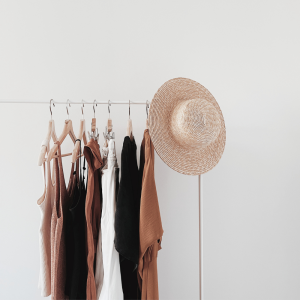 Wardrobe Organization. Clothes hanged up on the rail. White, beige, brown, black. And a straw hat i light beige